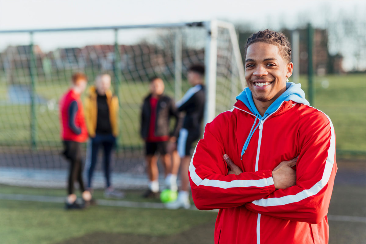 Young man training at a soccer field smiling at camera with friends in background