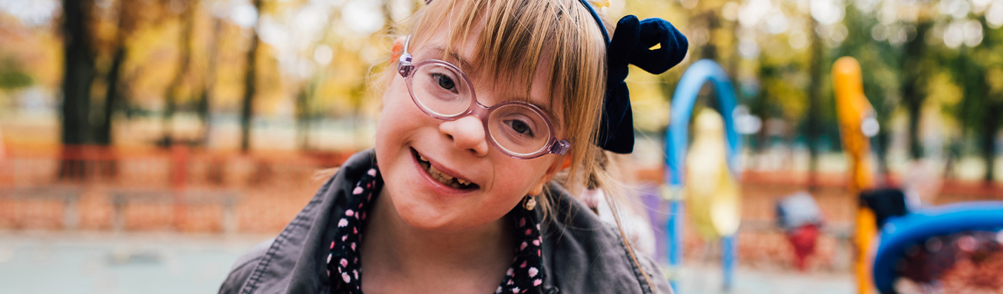 Young girl with Down Syndrome in playground smiling at camera