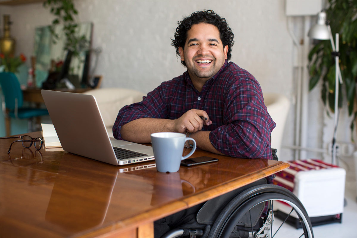 Vulnerable People Like this Man working at home on laptop using a wheelchair smiling at camera